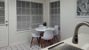 Una cocina moderna con encimera blanca, pileta de acero inoxidable y comedor con mesa y sillas blancas.
