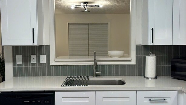 Una cocina moderna con armarios blancos, lavavajillas integrado, pileta de acero inoxidable y ventana sobre la pileta.