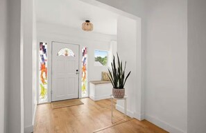 Ein Flur mit Holzboden, einer weißen Tür mit bleiverglastem Fenster und einer Topfpflanze auf einem kleinen Tisch.
