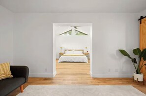 Ein Schlafzimmer mit einem Bett, einem Nachttisch, einem Fenster und einer Zimmerpflanze.