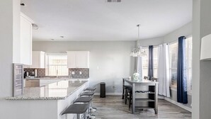 A modern kitchen with a central island, bar stools, and a dining area with a table and chairs.