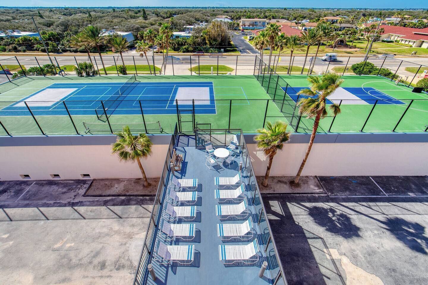 An outdoor tennis court with seating and palm trees.