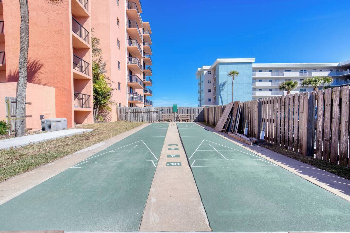 Un patio con una cancha de shuffleboard, rodeado de edificios de varios pisos con balcones y una valla de madera.