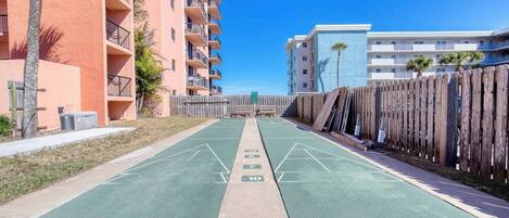 Un patio con una cancha de shuffleboard, rodeado de edificios de varios pisos con balcones y una valla de madera.