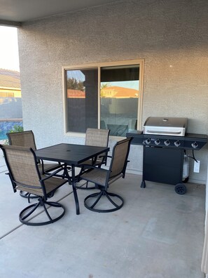 Eine Terrasse im Freien mit Tisch, Stühlen, einem Grill und einem Fenster.
