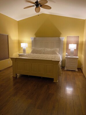 Ein Schlafzimmer mit einem Bett, zwei Nachttischen mit Lampen, einem Deckenventilator und Holzboden.