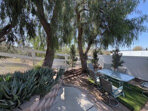 Un patio con mesa y sillas, rodeado de cactus y árboles.