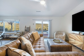 A modern living room with a leather sofa, a wooden cabinet, and a large TV. - Beautiful 3-bedroom house with AC in adorable Oakhurst, your own private retreat (Oakhurst)