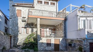 Ein zweistöckiges Steinhaus mit Balkon, einer Treppe und einem kleinen Garten.