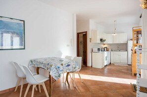 A modern kitchen with white cabinets and a dining area with a table and chairs. - La Vista Garden Apartment (Rovinj)