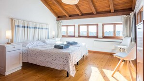 Une chambre avec un plafond en bois, un lit recouvert d’une housse à motifs à pois, un bureau, une chaise et une fenêtre avec des rideaux.