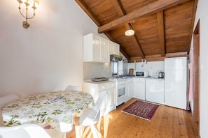 A compact kitchen with white cabinets, a stove, microwave, and a refrigerator. There's a wooden ceiling and a small dining area with a floral tablecloth. - La Vista Sea View Apartment 2 (Rovinj)