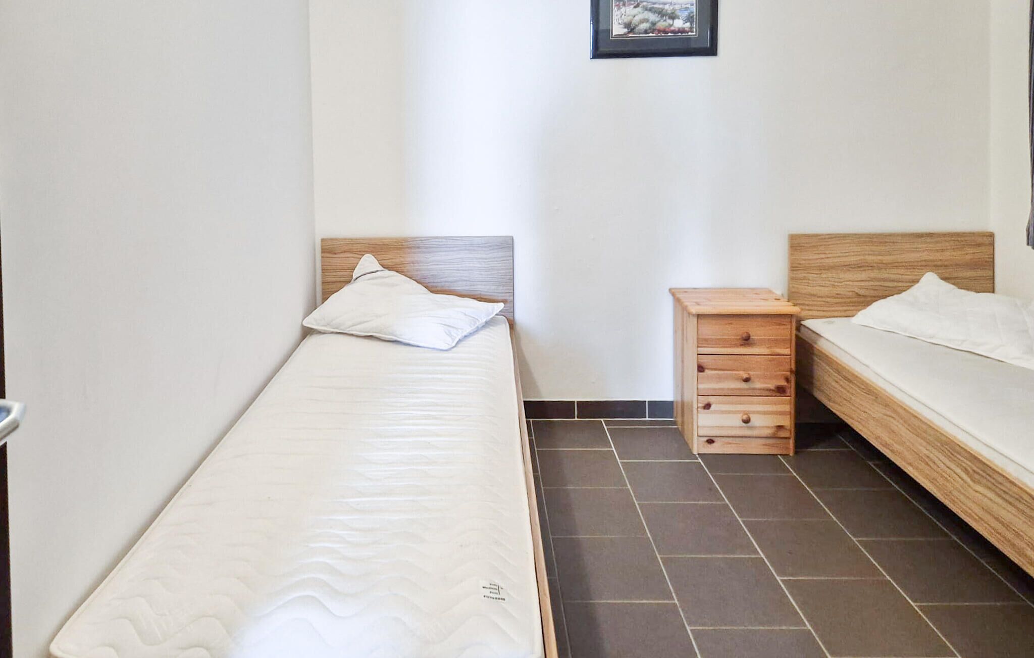 Ein kleines, sauberes Zimmer mit zwei Betten, einem Holznachtkästchen und Fliesenboden.