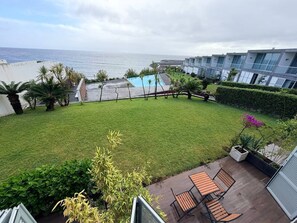 Une vue d’un jardin bien entretenu, avec une piscine, du mobilier de jardin et une vue sur l’océan.