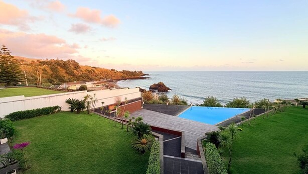 Una propiedad residencial con piscina, césped cuidado y vista al mar.