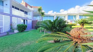 Un edificio moderno con varios balcones, un césped cuidado y plantas tropicales.