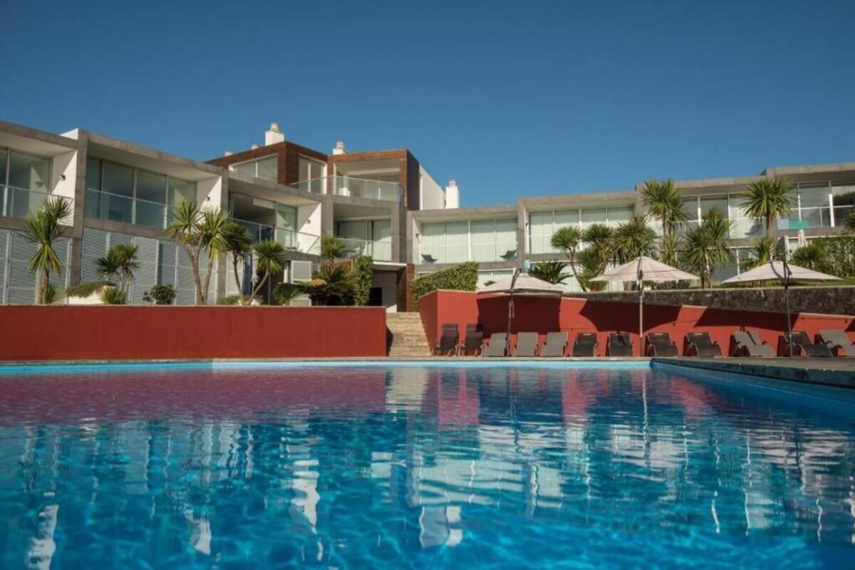 A modern hotel with a swimming pool, palm trees, and sun loungers.