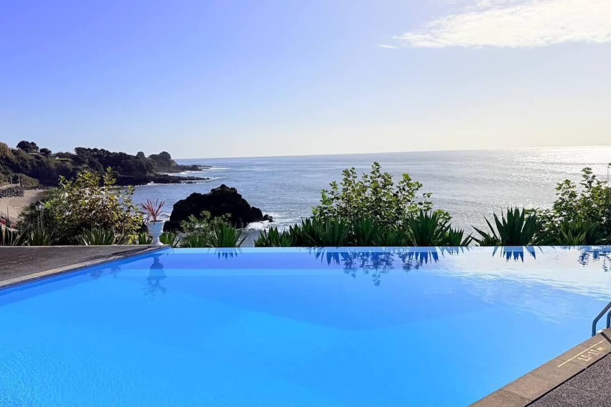 An infinity pool with a clear view of the ocean and a rocky coastline.