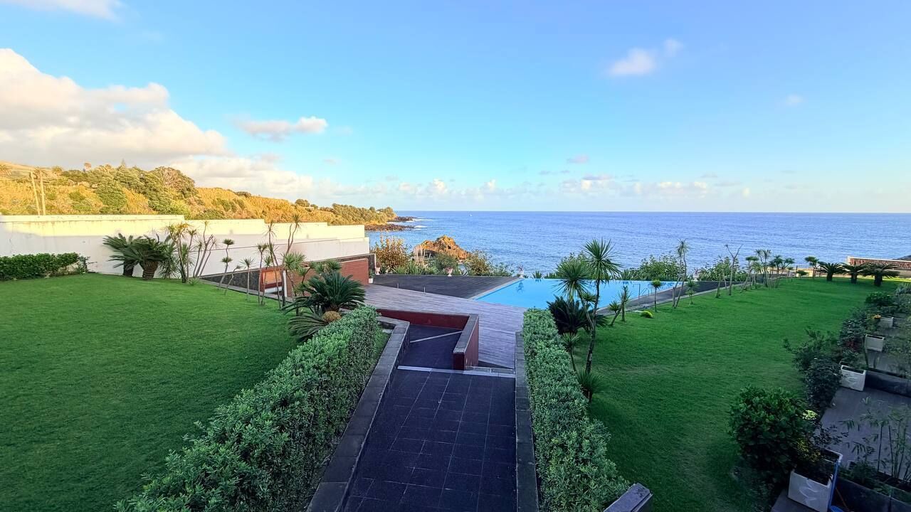 Um imóvel residencial com piscina, gramado bem cuidado e vista para o oceano.