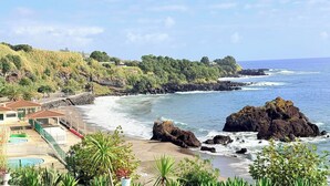 Un complejo turístico frente al mar con piscina, playa y afloramientos rocosos.