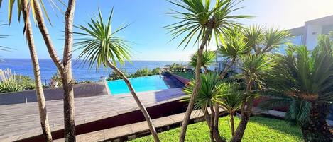 A pool area with a wooden deck, palm trees, and a view of the ocean.
