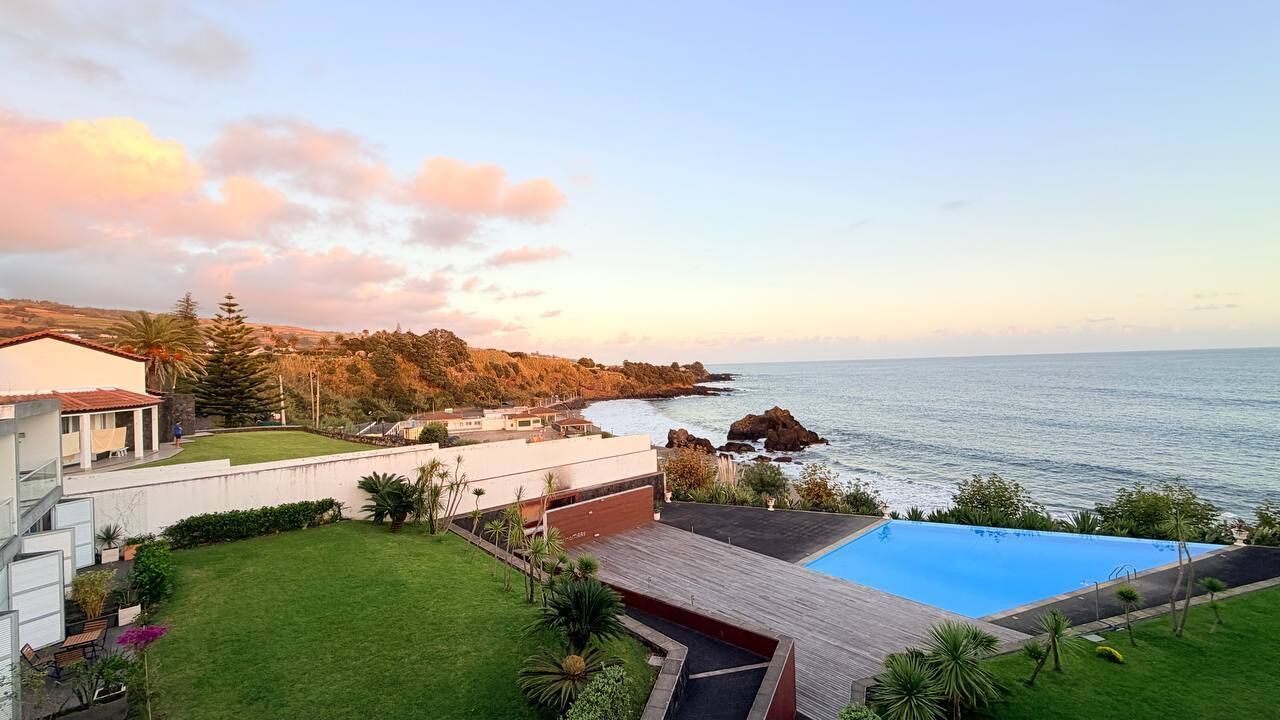 A coastal property with a swimming pool, a grassy lawn, and a view of the sea.