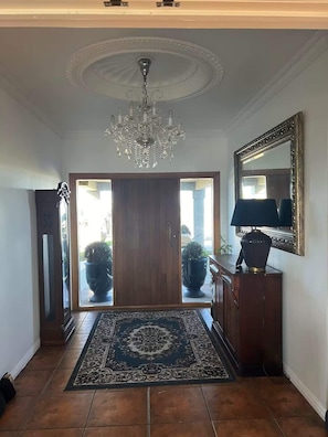 Un pasillo con candelabro, un espejo grande y una puerta de madera.