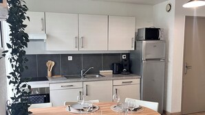 Ett modernt kök med vita skåp, en mikrovågsugn och ett kylskåp. Ett matbord är dukat med tallrikar, glas och bestick.