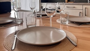 Ett matbord dukat med tallrikar, glas och bestick i ett modernt kök med skåp och ett fönster.