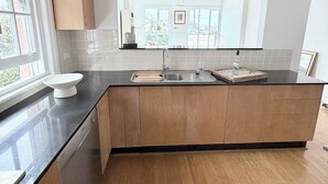 Cozinha moderna com armários de madeira, bancada preta e uma ampla janela com vista para a cidade.