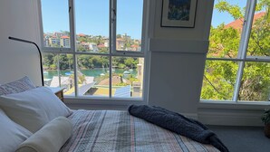Quarto com uma janela grande, cama com roupa de cama estampada e vista para um porto de iates e edifícios.