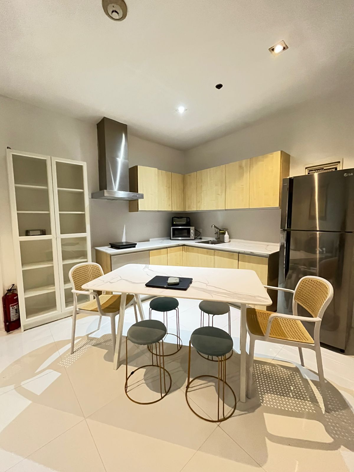Una cocina moderna con una isla central, armarios empotrados, un refrigerador de acero inoxidable y una zona de comedor con una mesa blanca y cuatro sillas.