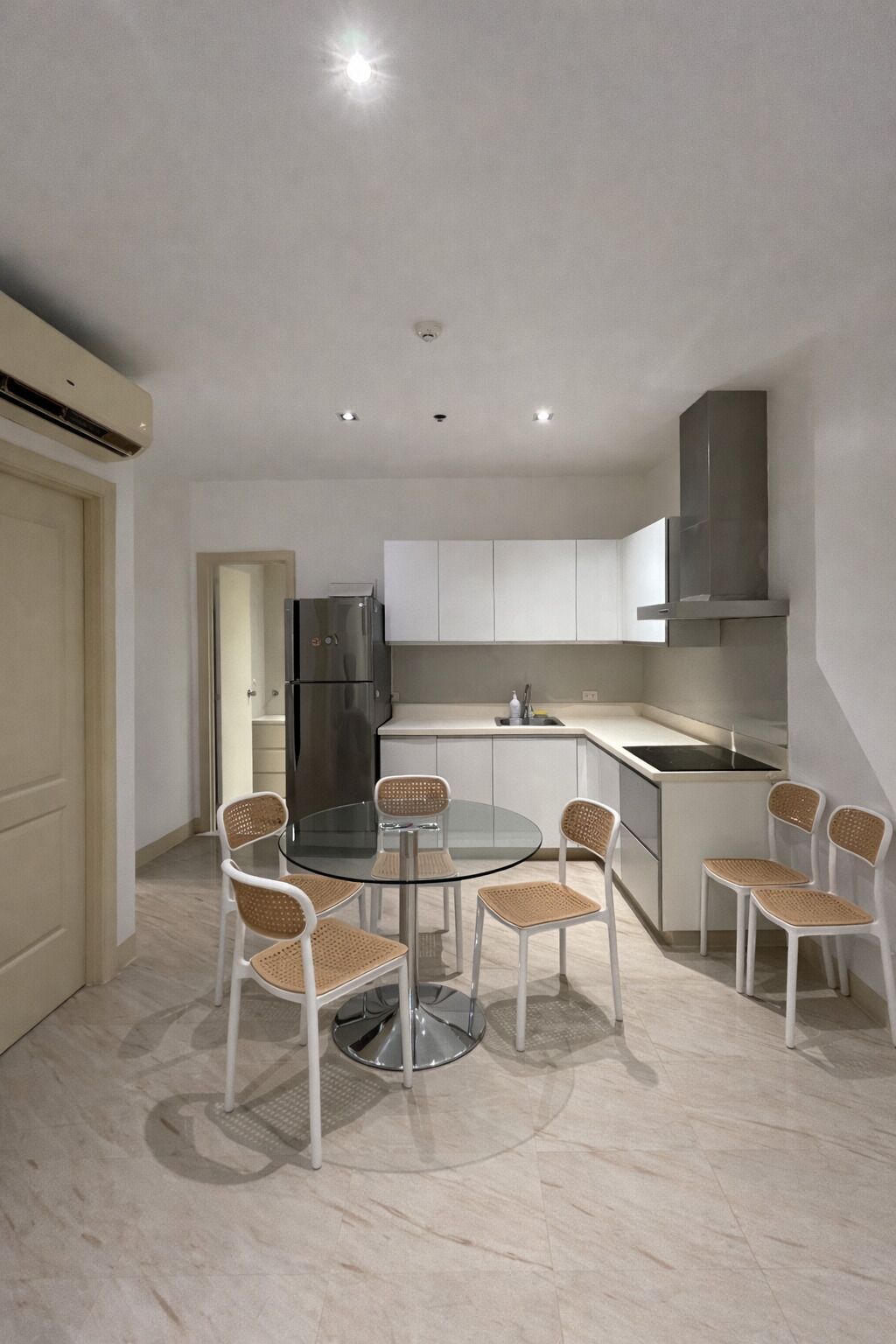 Una cucina moderna con mobili bianchi, un frigorifero in acciaio inossidabile e un tavolo rotondo in vetro con sedie in vimini.