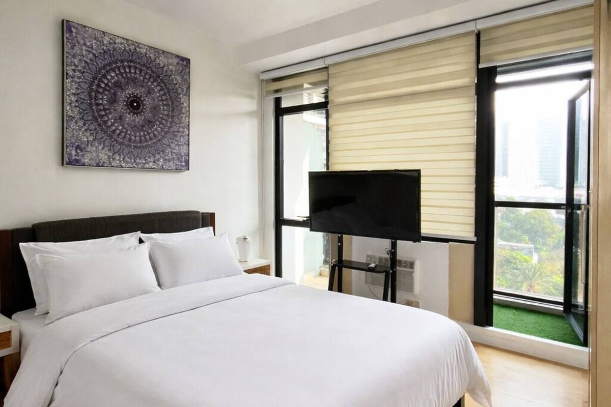 Una camera da letto con un letto grande, una TV a schermo piatto, una luce a soffitto e una finestra con tende.