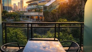 Un balcon avec une table et des chaises, donnant sur un paysage urbain composé d’immeubles modernes et illuminé par le coucher du soleil.