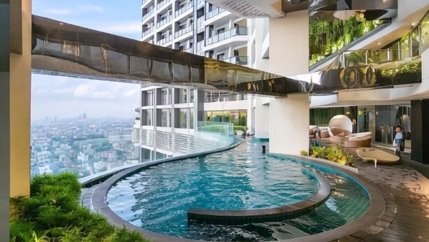 Une piscine à débordement située sur le toit, avec une bordure incurvée, entourée d’une végétation luxuriante et agrémentée de mobilier d’extérieur moderne.