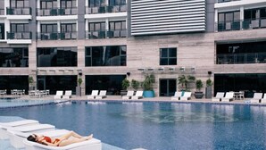 Un hotel moderno con piscina, sillones de descanso y un edificio de varios pisos con balcones.