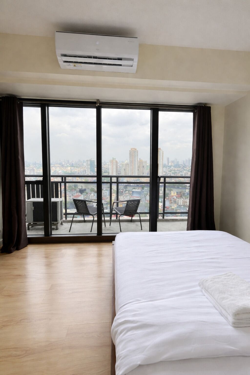 Une chambre d’hôtel avec un grand lit, un balcon avec deux chaises et une vue sur la ville.
