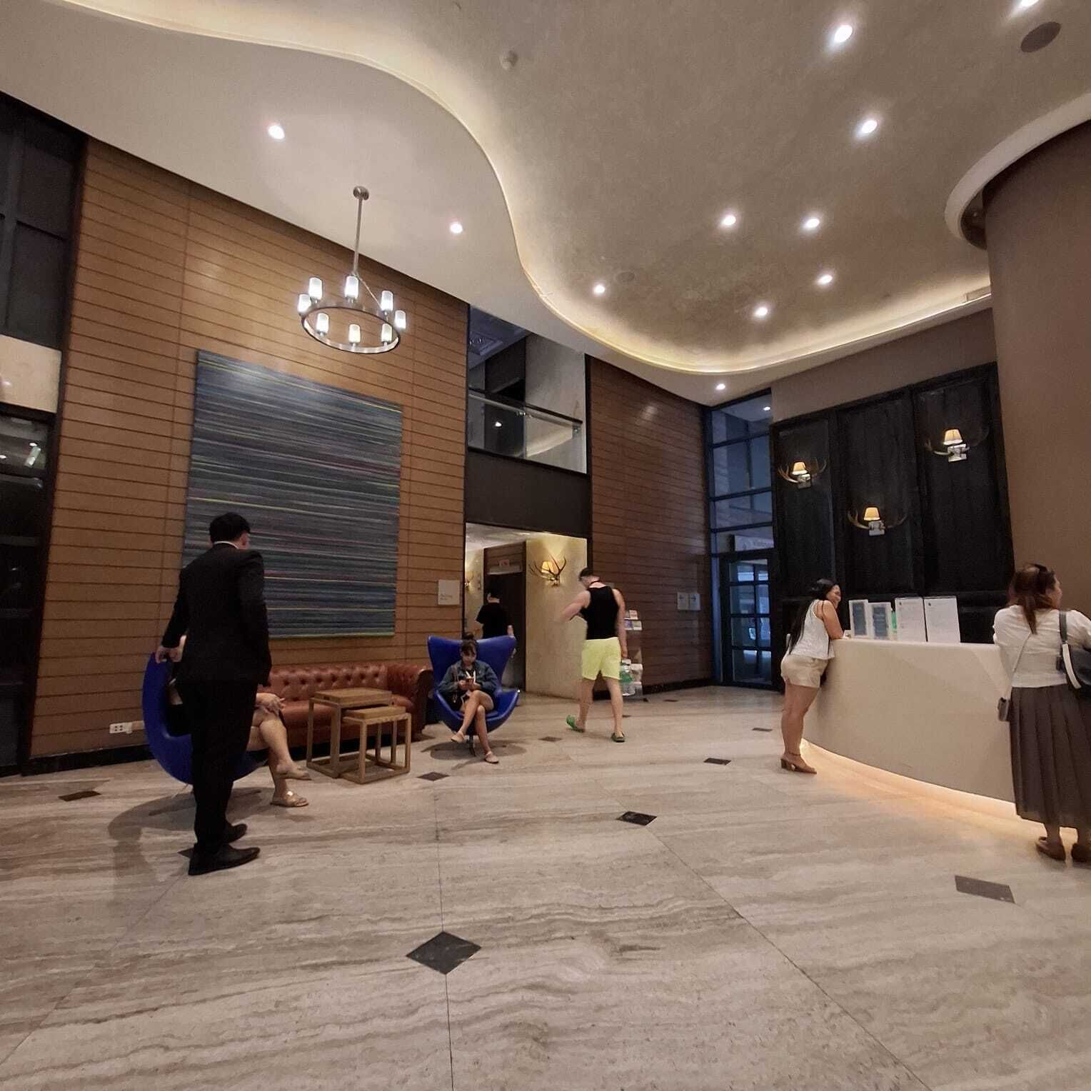 Eine Lobby mit gewölbter Decke, holzverkleideten Wänden, einem großen abstrakten Gemälde, einem Empfangstresen und einer Sitzecke mit einer Couch und Sesseln.