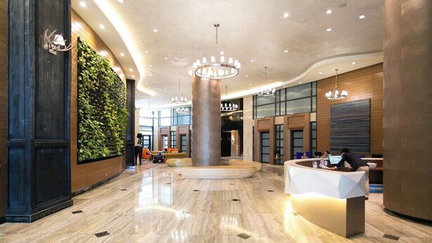 Un vestíbulo amplio con una recepción, un pilar grande y una pared verde con plantas.