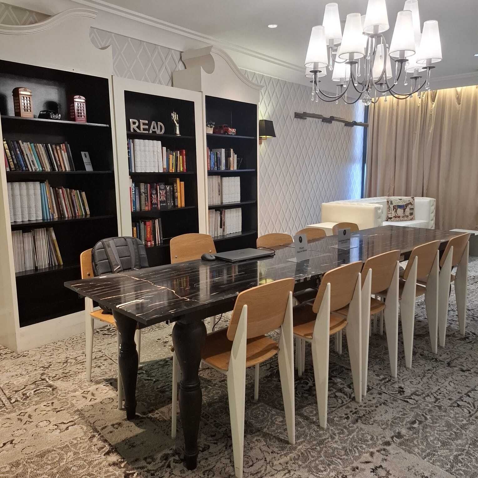 A dining area with a black table and white chairs, surrounded by bookshelves filled with books.
