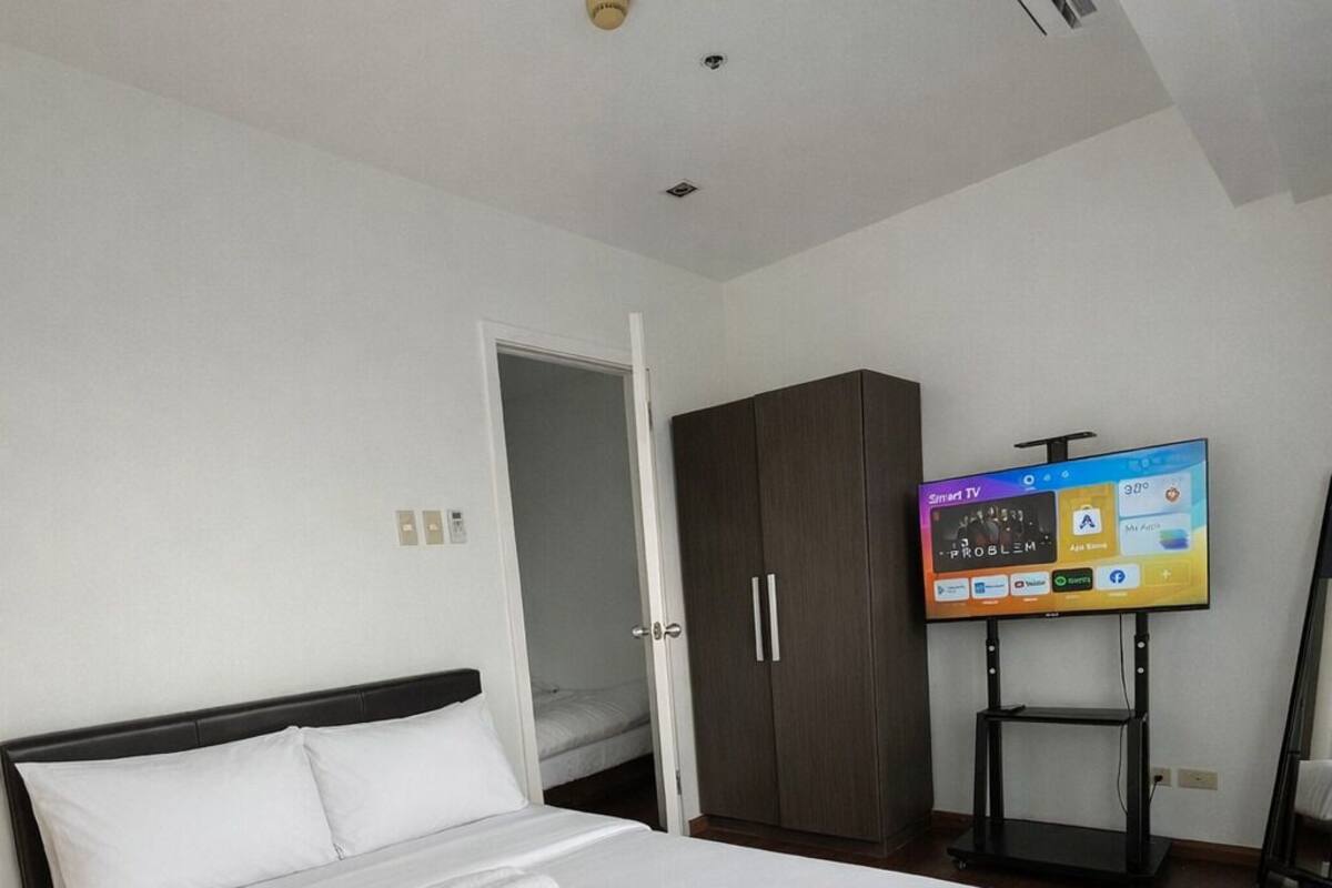 A modern hotel room with a large bed, a wardrobe, a television, and a desk.