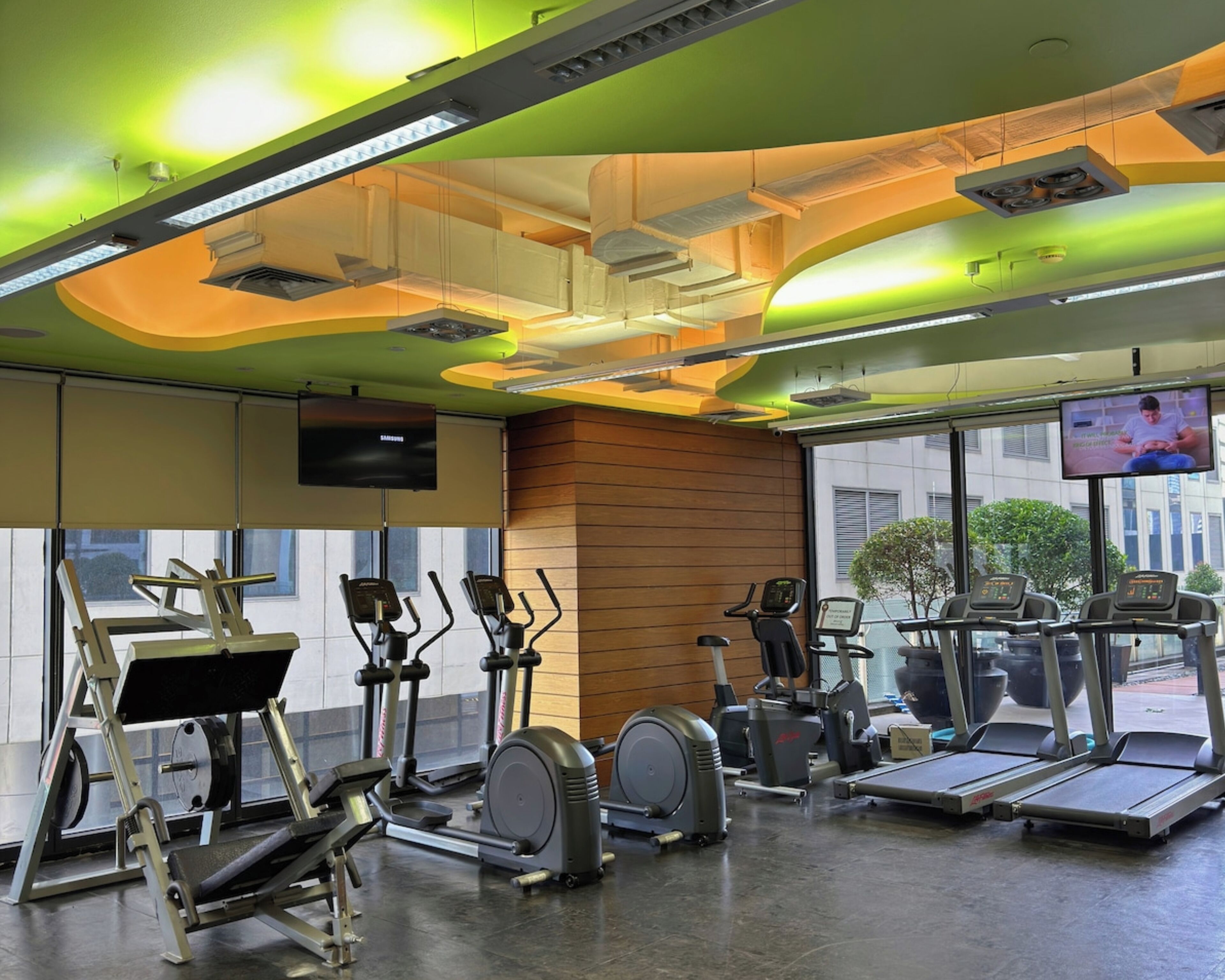 Un gimnasio con equipo de ejercicio variado, incluyendo cintas de correr y elípticas, y un televisor montado en la pared.