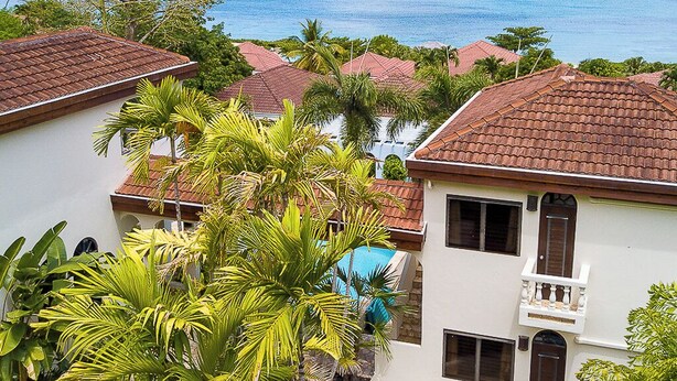 A coastal residential area with houses featuring red-tiled roofs and white walls, surrounded by lush greenery and a clear view of the ocean. - Stunning Vacation Villa Rental in the British Virgin Islands (Mahoe Bay)