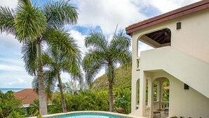 A swimming pool with tropical plants, a white building with arches, and a clear blue sky. - Stunning Vacation Villa Rental in the British Virgin Islands (Mahoe Bay)