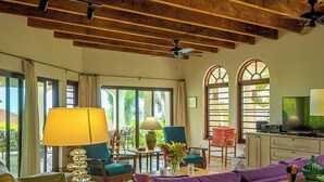A well-lit living room with a sofa, a coffee table, a lamp, and a television. There are windows with curtains, a ceiling fan, and a view of the outdoors. - Stunning Vacation Villa Rental in the British Virgin Islands (Mahoe Bay)