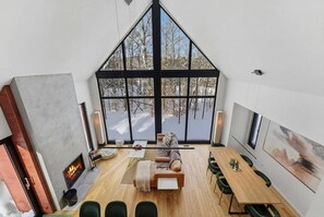 A modern interior with a large window, a fireplace, a dining area, and a cozy seating space. - Bright 4BR Sunlit Chalet Hot Tub & Fireplace (Lac-Supérieur)