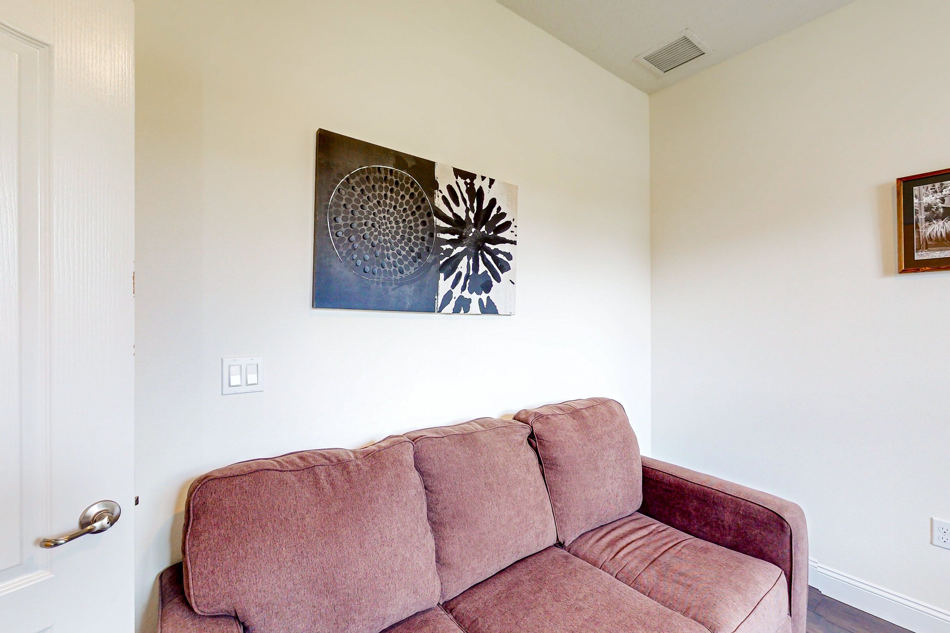A living room with a brown sofa, a wall-mounted abstract art piece, and a framed picture on the wall.