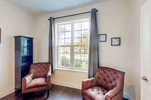 Ein Zimmer mit zwei braunen Ledersesseln, einem dunkelblauen Schrank und einem großen Fenster mit Vorhängen.
