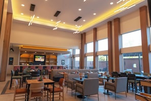 Un restaurante espacioso con techos altos, iluminación moderna y ventanas grandes.